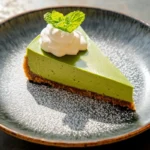 Sliced matcha cheesecake with a graham cracker crust and whipped cream.